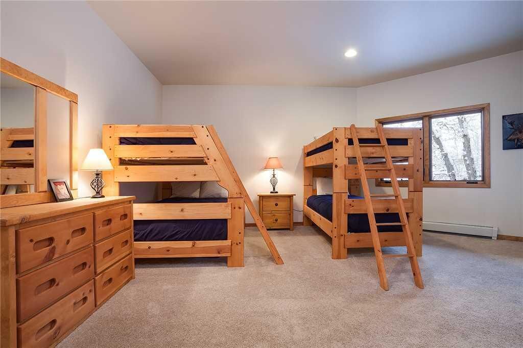 A room with two bunk beds, a dresser with drawers, a mirror, a bedside table with a lamp, and a window with a view of trees.