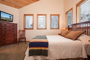 A bedroom with a bed, a dresser, a chair, and three windows.