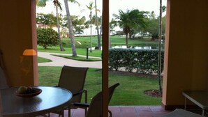 Un patio con mesa y sillas, un frutero y vistas a un jardín ajardinado con palmeras y una fuente de agua.