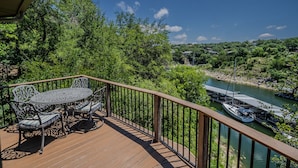 Eine Holzterrasse mit Tisch und Stühlen, mit Blick auf einen Fluss, auf dem Boote fahren, und eine bewaldete Landschaft.