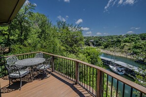 Eine Holzterrasse mit Tisch und Stühlen, mit Blick auf einen Fluss, auf dem Boote fahren, und eine bewaldete Landschaft.
