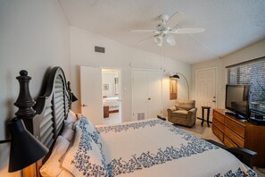A bedroom with a bed, a chair, a TV, and a ceiling fan.
