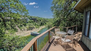 A wooden deck with a table and chairs, overlooking a river and greenery. - Luxury Lakehouse in striking distance to Austin with pool [#8 Rainbow Cactus] (Lakeway)