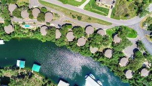 An aerial view of a lakeside property with a swimming pool, multiple circular structures, and a road. - Cool Treehouse Cabin for wake sport and boating with cave pool [#12 Honeysuckle] (Lakeway)