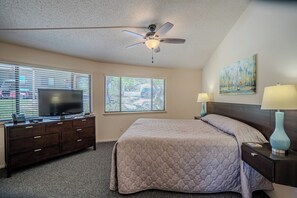 A bedroom with a bed, a desk with a TV, a ceiling fan, and two windows with blinds. - Honeysuckle #12 - Elevated Villa with Resort Pool (Lakeway)