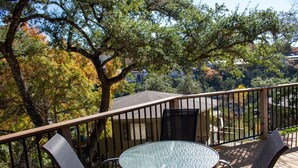 A deck with a round glass table and two chairs, surrounded by a wooden railing. - Relaxing Lakeview Treehouse btwn Austin & San Antonio with jacuzzi [#18 Yucca] (Lakeway)