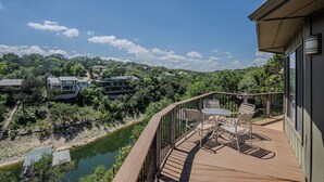 A wooden deck with outdoor furniture overlooking a river and a forested area. - Treehouse Crash Pad for watersport on Lake Travis [#13 Texas Star] (Lakeway)