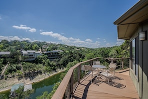 A wooden deck with outdoor furniture overlooking a river and a residential area. - Texas Star #13 - Treehouse Retreat with Pool Access (Lakeway)