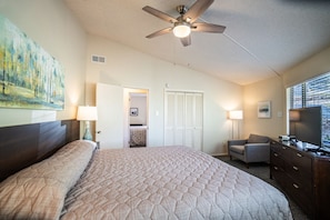 A hotel room with a bed, a desk, a chair, a ceiling fan, and a television.