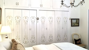 Ein Schlafzimmer mit Bett, Lampe, Sessel, einer Deckenleuchte und einem Kleiderschrank mit Verzierungen.