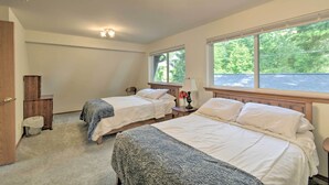 Une chambre avec deux lits, une tête de lit en bois, une table de chevet, une lampe et une fenêtre donnant sur des arbres.