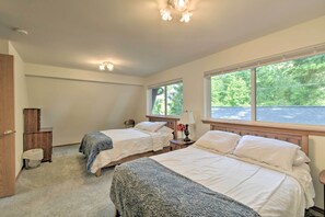 Une chambre avec deux lits, une tête de lit en bois, une table de chevet, une lampe et une fenêtre donnant sur des arbres.