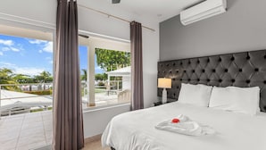 Une chambre d’hôtel avec un grand lit, une fenêtre avec des rideaux, une table de chevet avec une lampe et un appareil de climatisation.