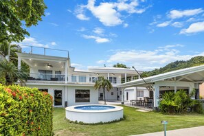 Una casa moderna de dos pisos con un patio cubierto, piscina y abundante vegetación.