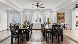 Un espace repas comprenant une grande table, plusieurs chaises, un ventilateur de plafond et un tapis à motifs de pierre.