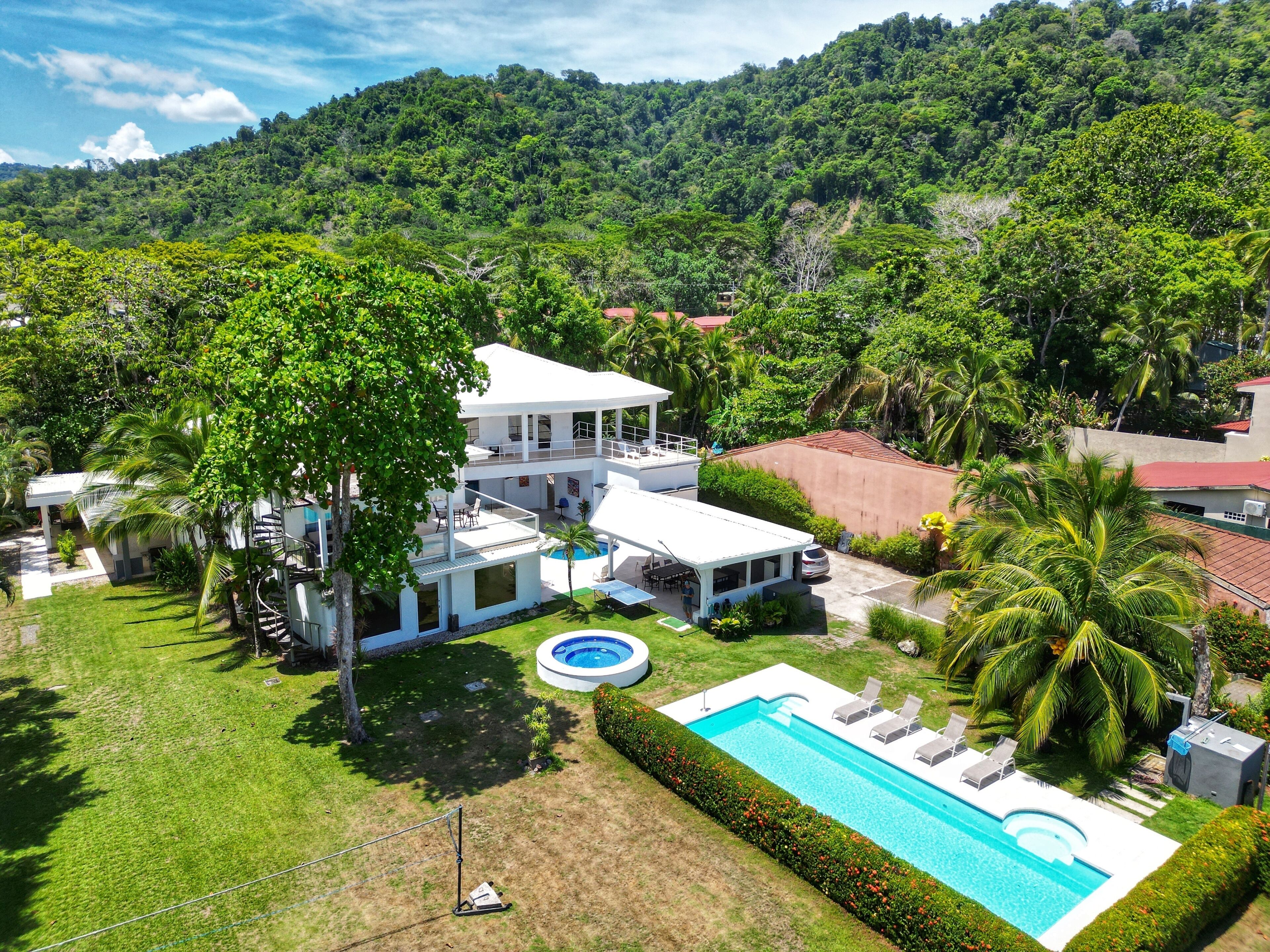 A two-story house with a pool, surrounded by lush greenery and hills.