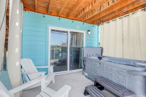 Un patio cubierto con un jacuzzi, sillas Adirondack blancas y un ventanal corredizo que da a una zona de piscina.