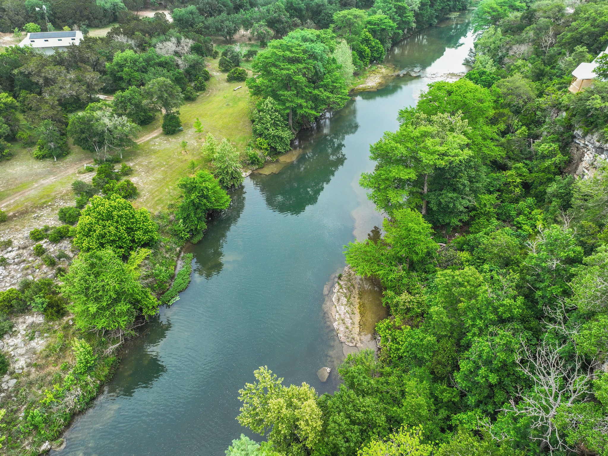 A river winding through a densely wooded area with a small building on the left bank.