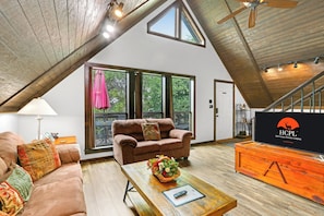 A spacious living area with a high ceiling, large windows, and a cozy seating arrangement.