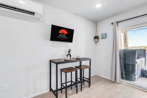 Una habitación moderna con una mesa de comedor, dos taburetes de bar, un televisor montado mostrando un logotipo y vistas a un lago a través de una puerta corredera de vidrio.