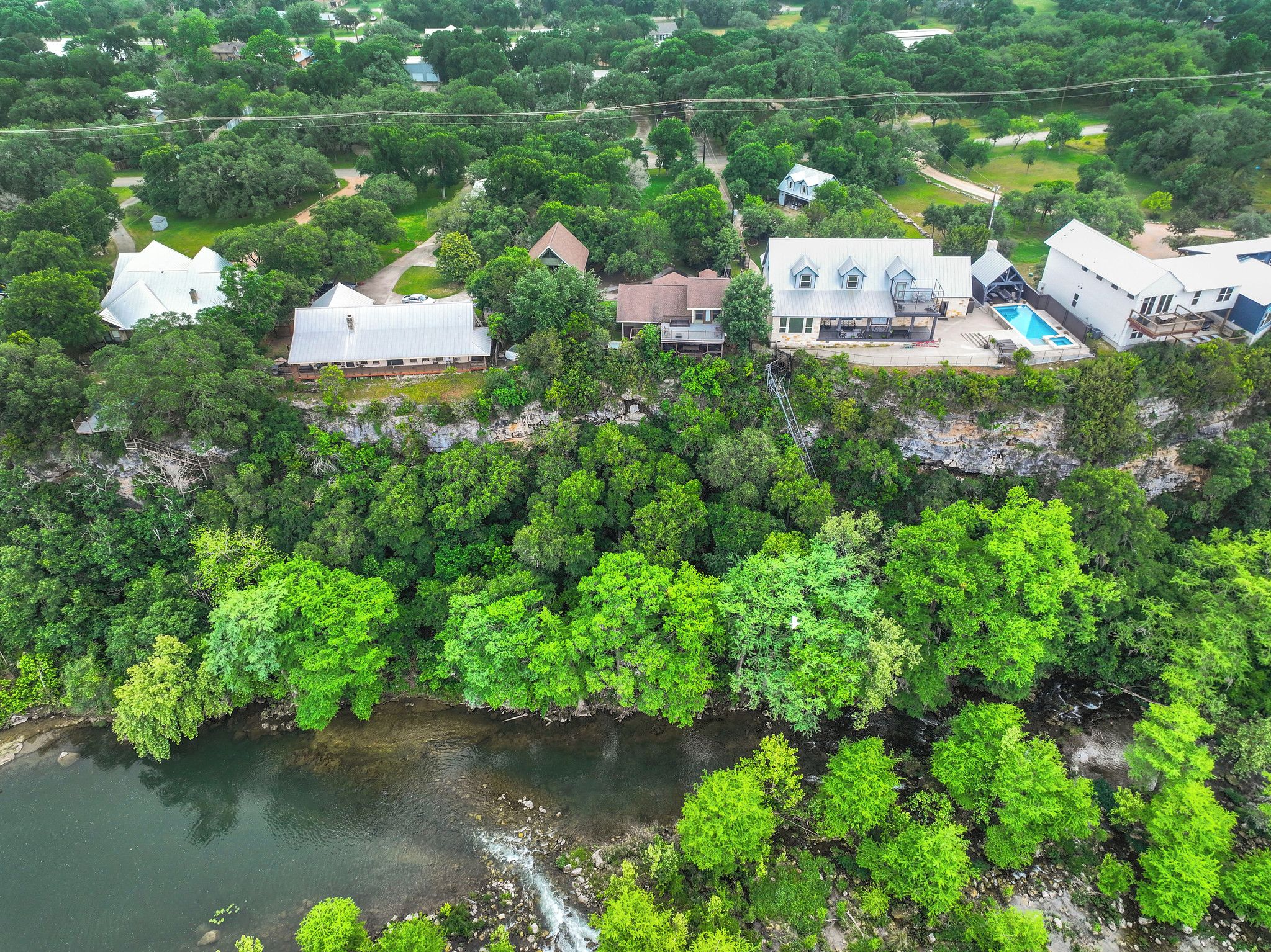 An aerial view of a residential area with houses, a swimming pool, and a river.