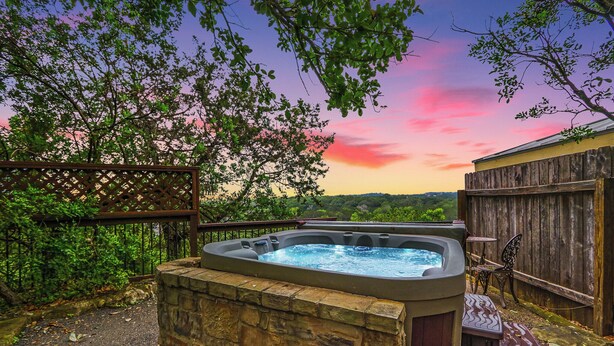 A hot tub with stone walls, a wooden fence, and a view of a sunset.