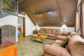 A spacious loft with a high ceiling, wooden beams, a sofa set, a coffee table, and a fireplace.