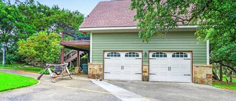 A two-story house with a green exterior and a red roof, featuring two garage doors and a small porch.