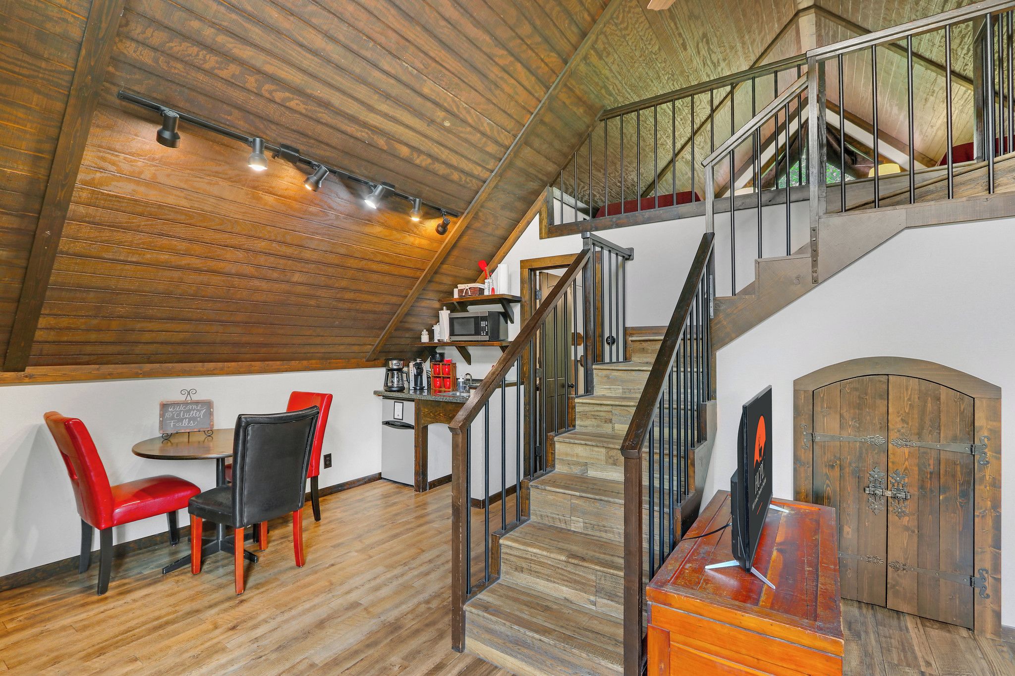Un loft spacieux avec un plafond en bois, un escalier doté de rampes en métal et un coin repas avec des chaises rouges.