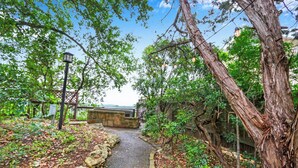 A pathway flanked by trees and a stone wall, leading to a building with a view.