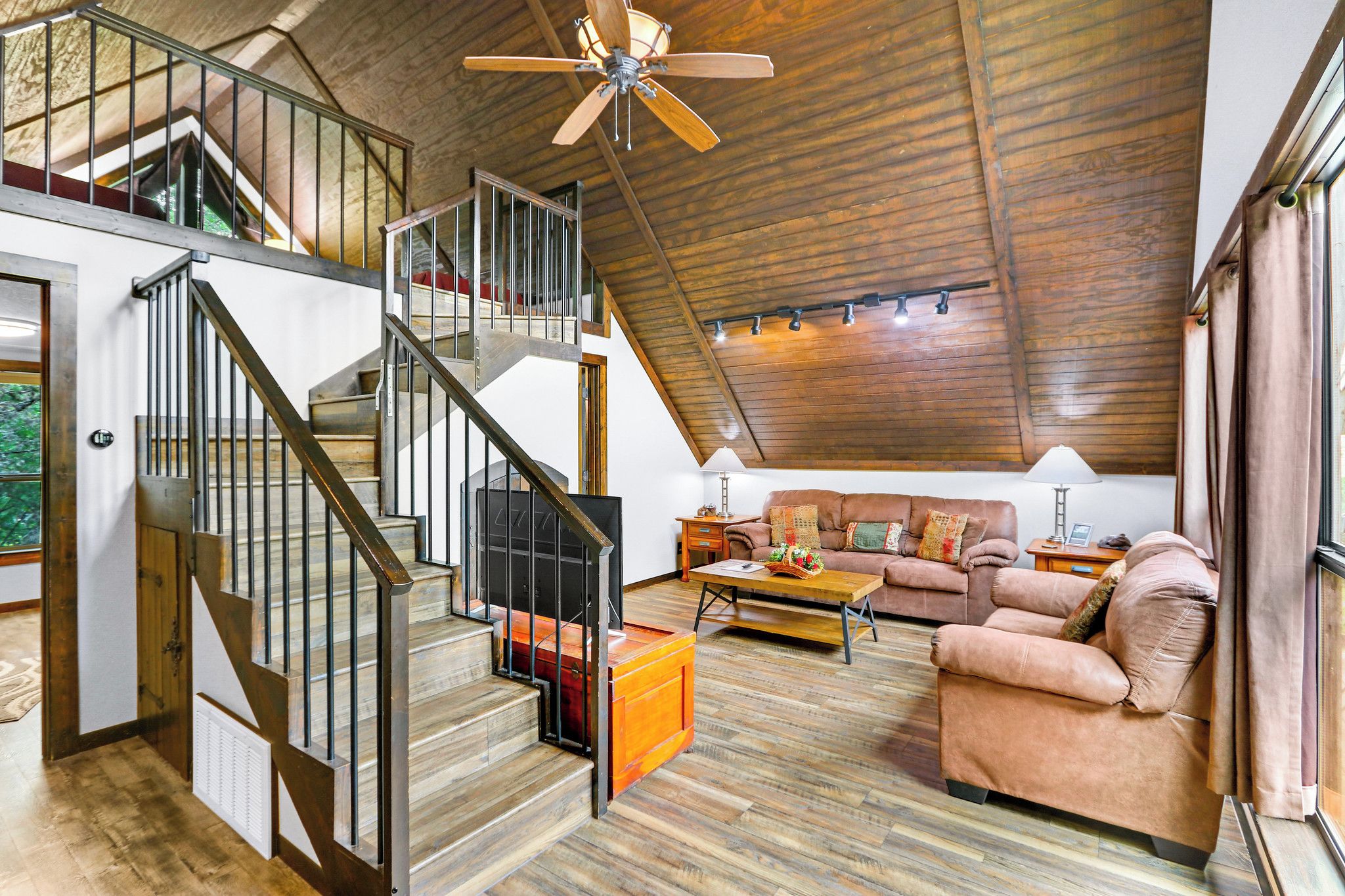Un loft spacieux avec un escalier en bois, un salon confortable doté d’un canapé et d’une table basse, et un ventilateur de plafond.