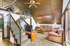 Un loft espacioso con escalera de madera, una zona de estar acogedora con sofá y mesa de centro, y un ventilador de techo.