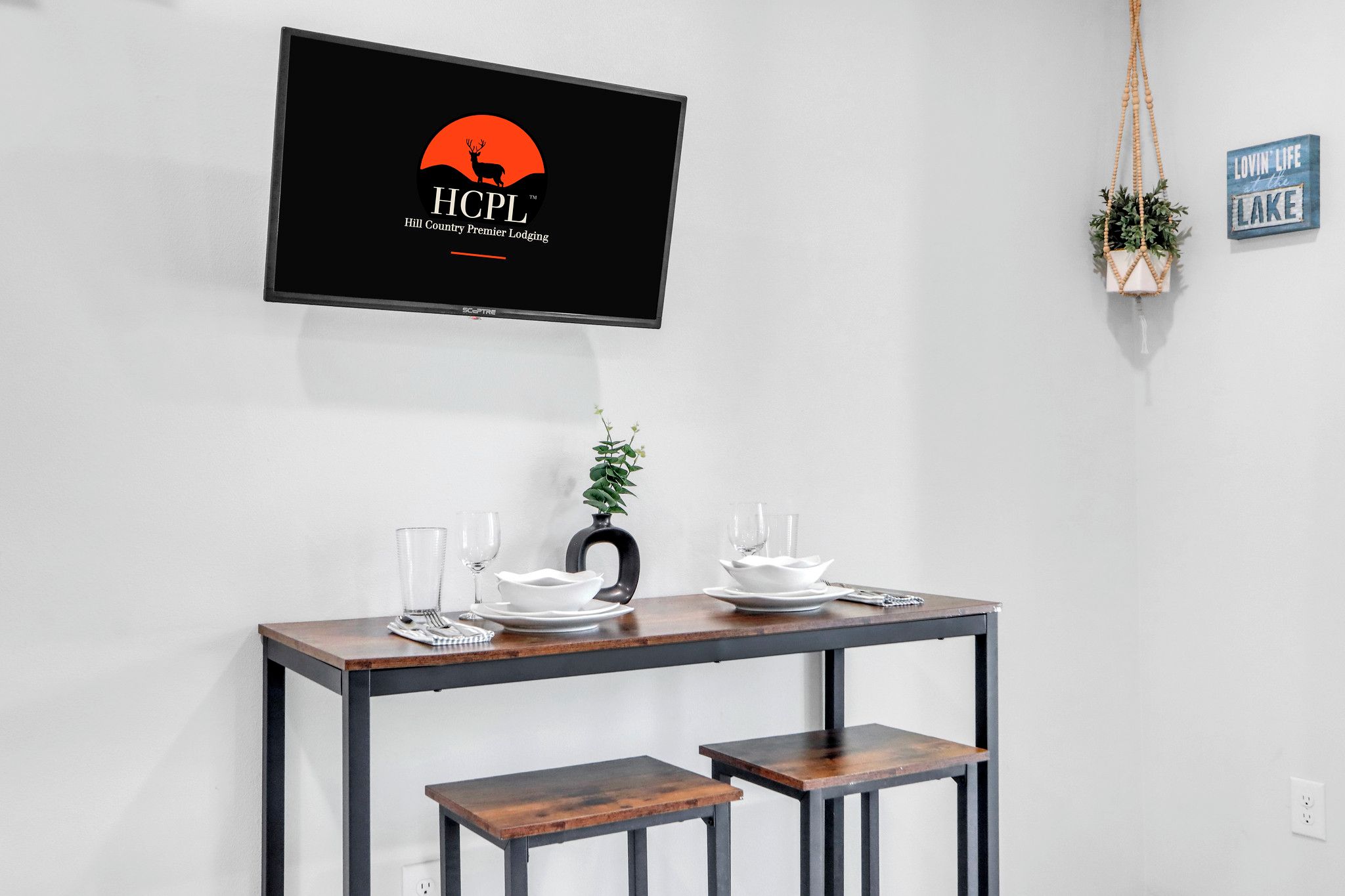 A dining table with a TV displaying the HCPL logo, a potted plant, and a sign saying "lovin' life at Lake".