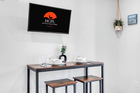 A dining table with a TV displaying the HCPL logo, a potted plant, and a sign saying "lovin' life at Lake".