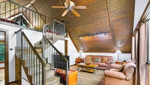A spacious living area with a wooden ceiling, a staircase with metal railings, a sofa set, and a coffee table.