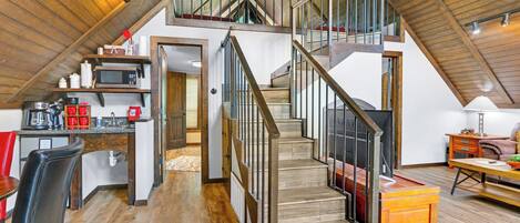 A spacious loft with a high ceiling, a wooden staircase, and a kitchen area with modern appliances.