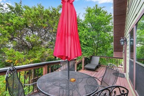 Une terrasse avec une table ronde et des chaises, un parasol rouge et une vue sur les arbres.