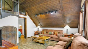 A spacious loft with a high ceiling, wooden beams, a cozy seating area with a sofa and armchairs, a wooden coffee table, and a fireplace.