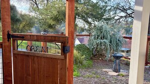 A wooden pergola with a sliding gate, a stone pathway, and a garden with trees and a birdbath.