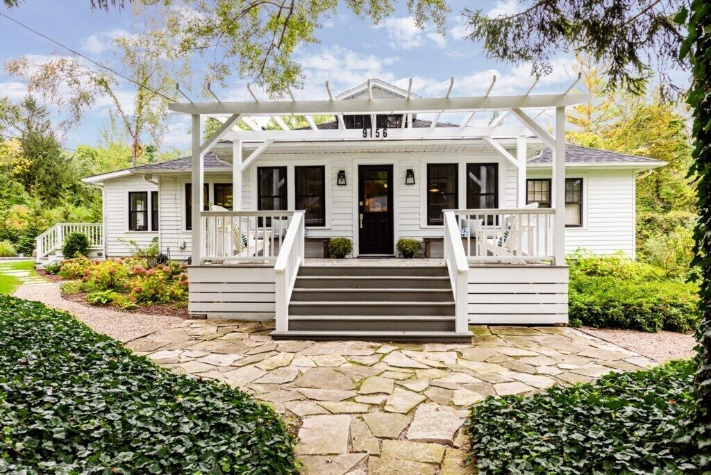 A white house with a porch, stone steps, and a number 9156 on the front door.