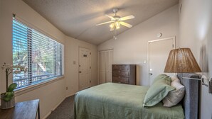 Ein Schlafzimmer mit einem Bett, einem Schminktisch, einer Lampe, einem Deckenventilator und einem Fenster mit Jalousien.
