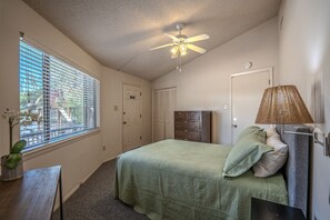 A bedroom with a bed, a dresser, a lamp, a ceiling fan, and a window with blinds.