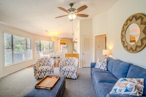 A living room with a sofa, two patterned armchairs, a coffee table, a ceiling fan, and a kitchen area in the background. - Midweek waterfront heaven near Austin with pool and hot tub [#5 Rain Lily] (Lakeway)