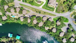 An aerial view of a lakeside property with a circular dock area, a road, and a building with a sloped roof.