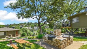 A backyard with a stone fire pit, a wooden picnic table, and a covered seating area.