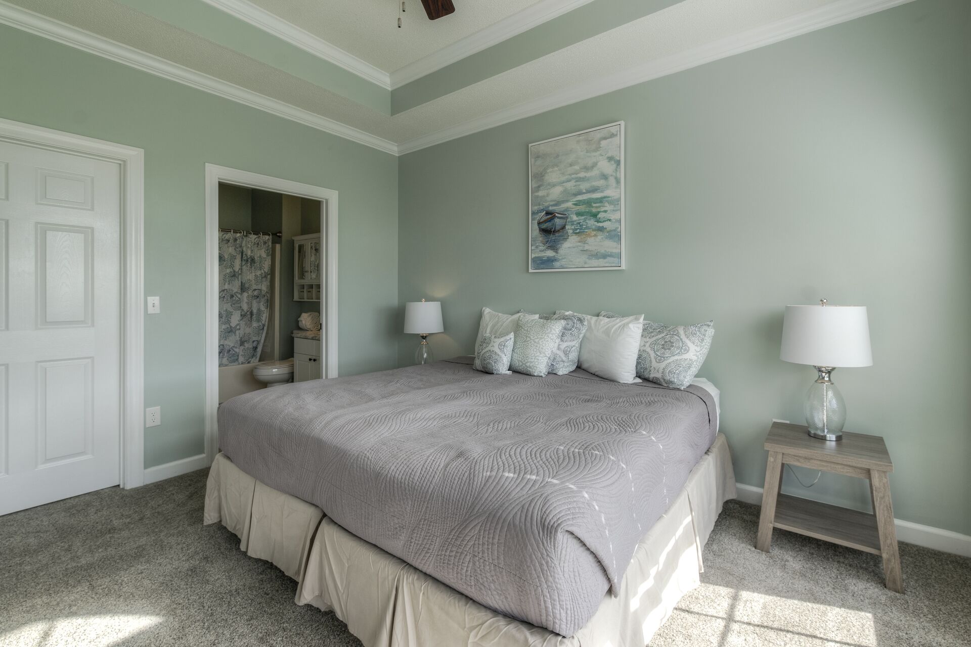 A bedroom with a bed, two bedside tables, a nightstand, a painting, and a door.
