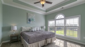 Ein Schlafzimmer mit einem Bett, einem Nachttisch, einer Lampe, einem Deckenventilator und einem großen Fenster mit Jalousien.