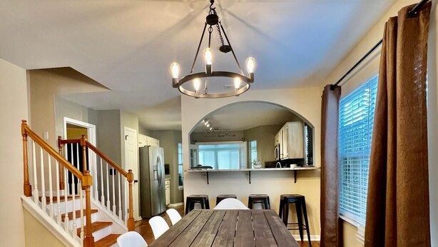 A dining area with a wooden table and white chairs, a chandelier, and a staircase leading to another room. - Luxurious Franklin Experience! 5min To Downtown   (Franklin)
