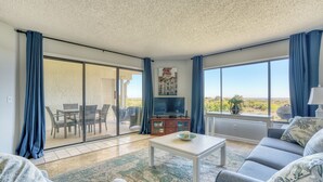 Un salon spacieux comprenant un canapé, une table basse et un téléviseur. Une porte-fenêtre coulissante donne accès à un espace extérieur aménagé avec des chaises et une table.
