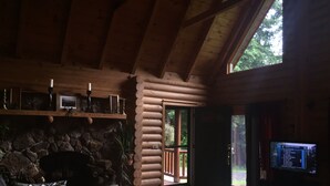 A log cabin interior with a stone fireplace, a large window, and a television. - perfect getaway near sylvan beach! 2 night minimum (Blossvale)